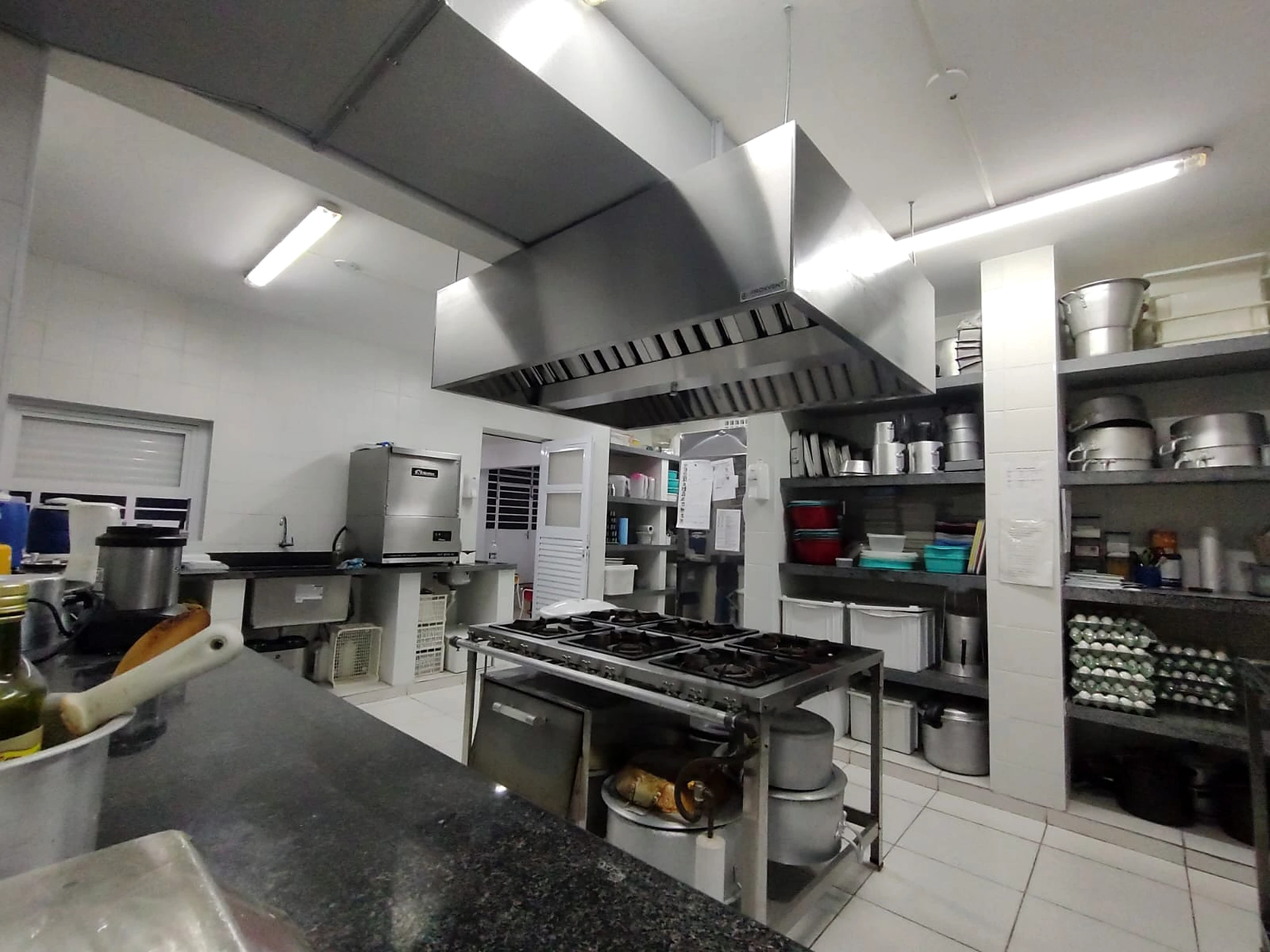 Coifa de ilha em aço inox sobre linha de cocção de cozinha profissional