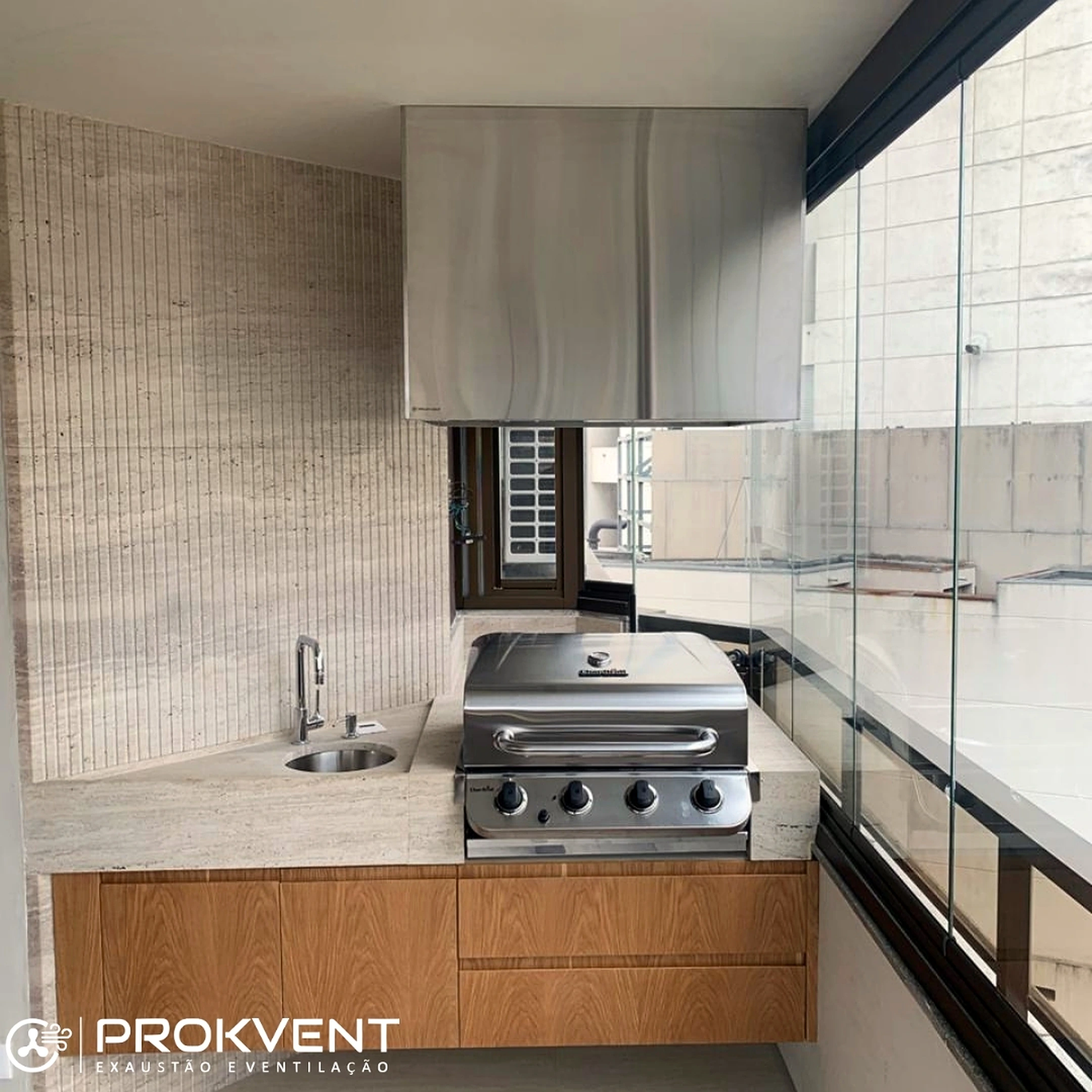 Coifa residencial em inox instalada sobre churrasqueira em varanda gourmet